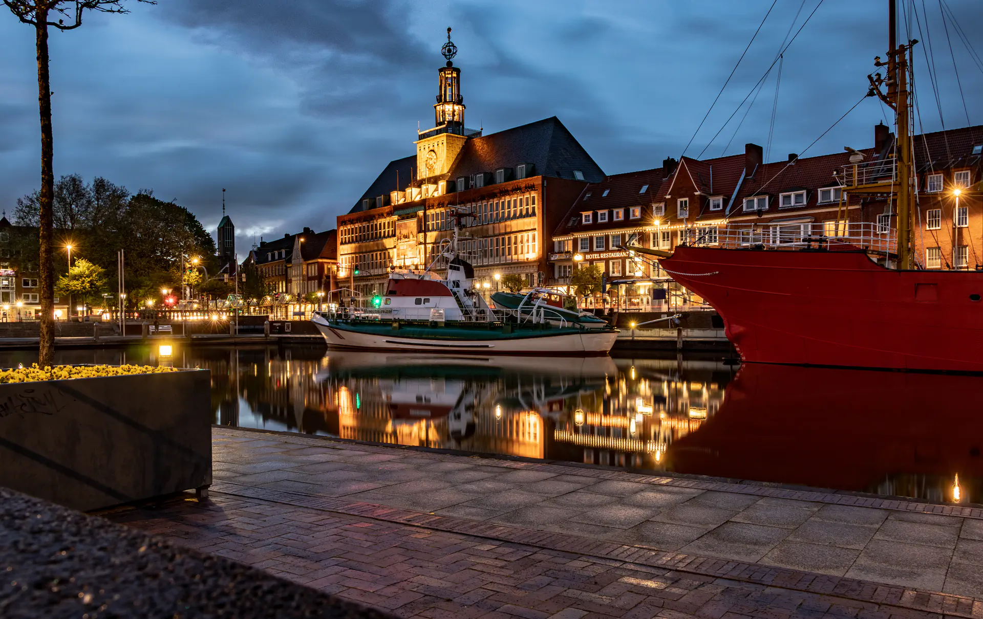Emden Hafen bei Dämmerung mit beleuchtetem Rathaus, Schiffen und Spiegelungen im Wasser.